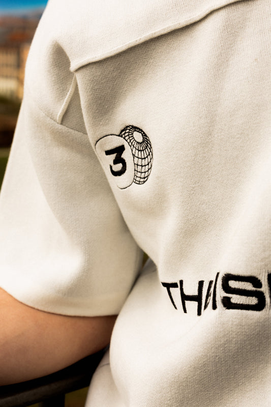 Close-up of a person wearing a beige shirt with a logo and text on the sleeve.